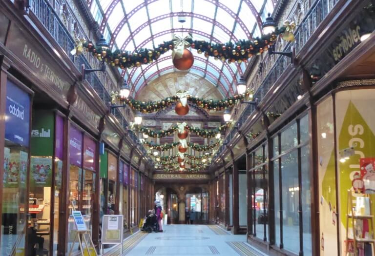 Two rows of shops inside of Central Arcade, with Christmas decorations hanging from the ceiling.